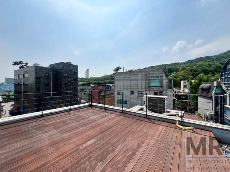 Rooftop deck overlooking neighboring buildings and a green hill