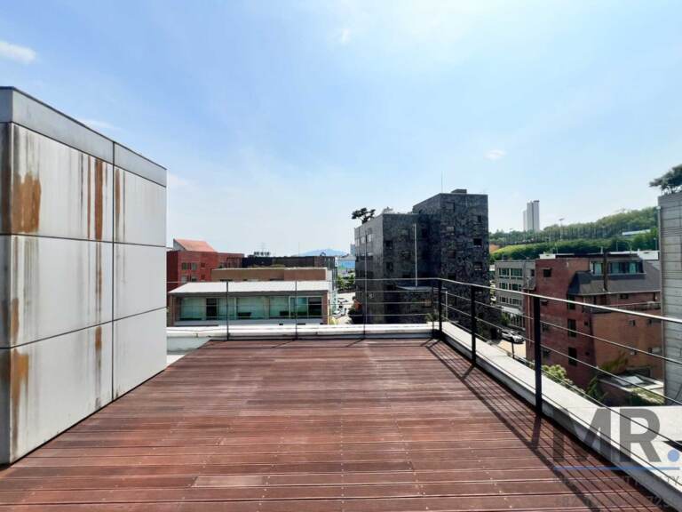 Wide wooden rooftop deck with railing and city view