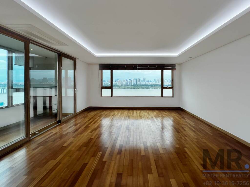Empty living area with dark wood floor and windows facing the river