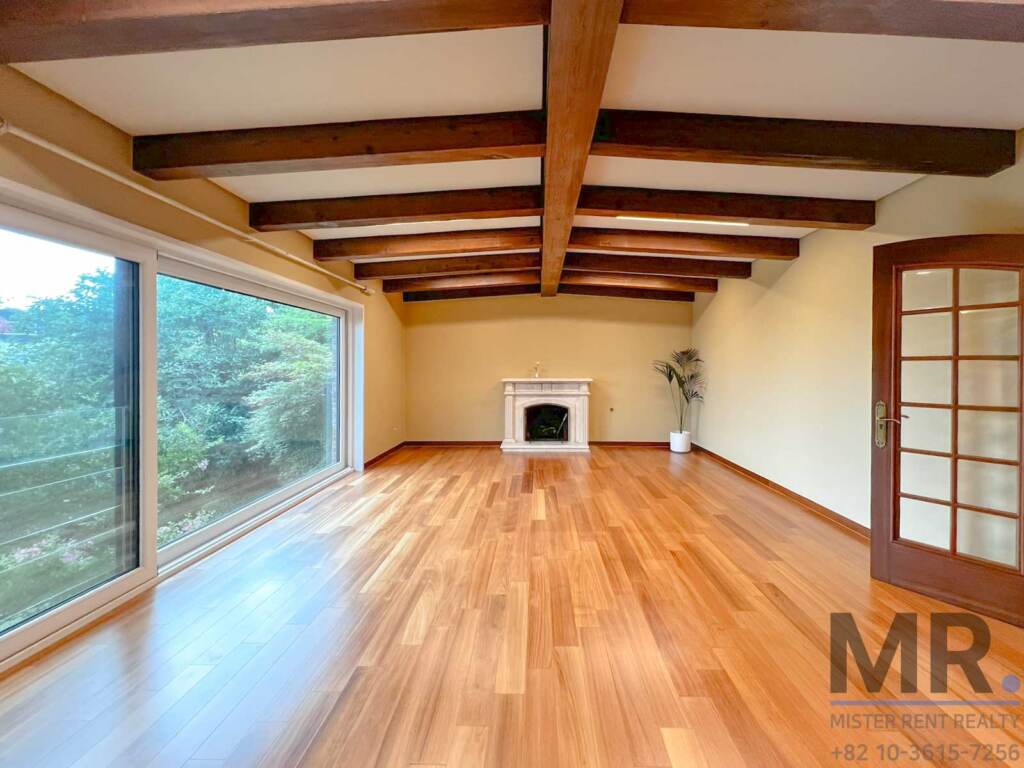 Living room with exposed wooden beams, fireplace and wide windows overlooking trees