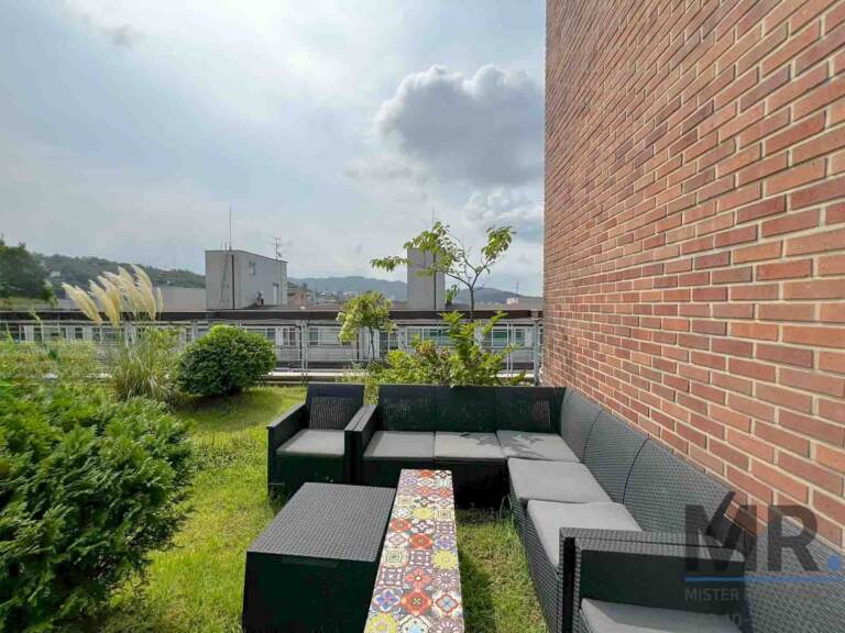 Rattan sectional sofa with tiled coffee table beside a brick wall on the rooftop