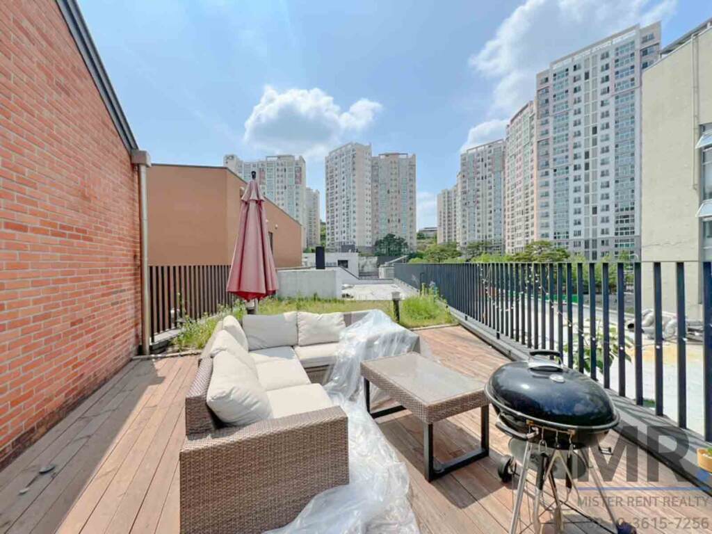 Rooftop terrace with wicker sofa, grill and apartment towers beyond