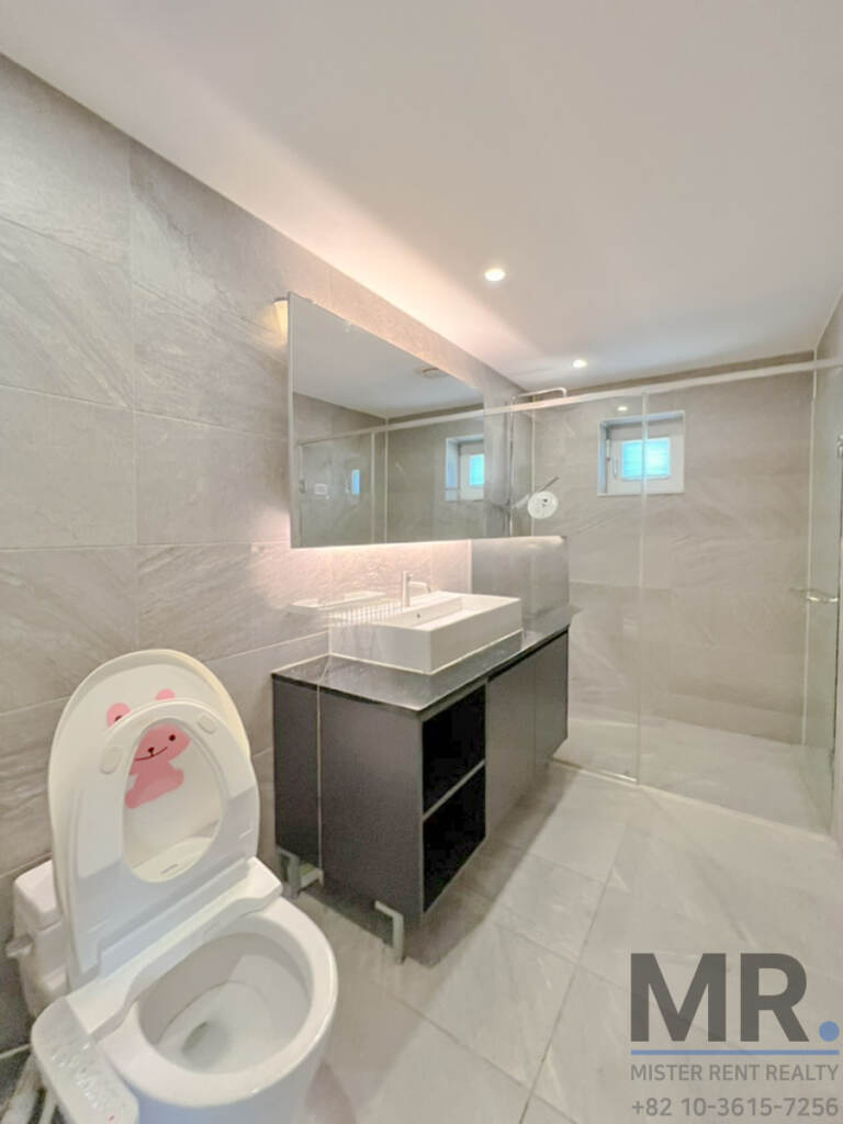 Grey-tiled bathroom with dark vanity and glass shower