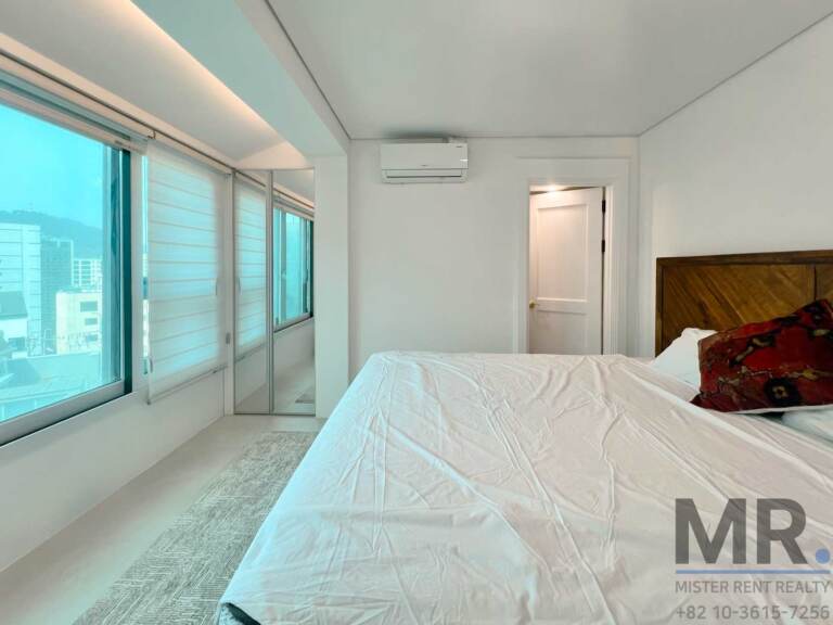 Master bedroom with wooden headboard and windows overlooking the city