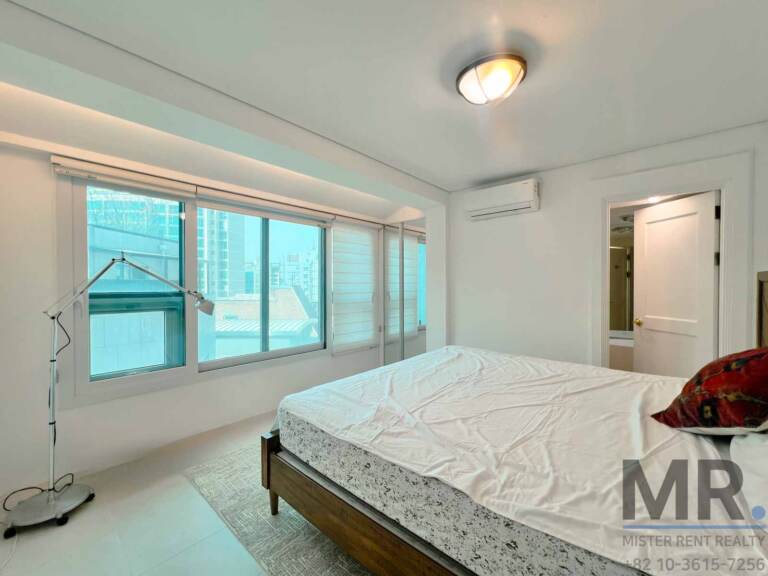 Bedroom with queen bed, wall air conditioner and city-view windows