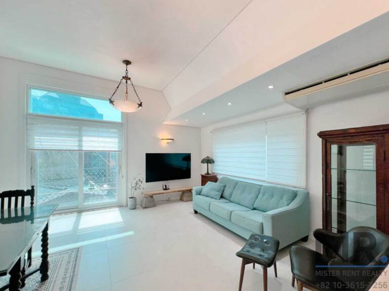 Lounge area with teal sofa, TV and high window with roller blinds