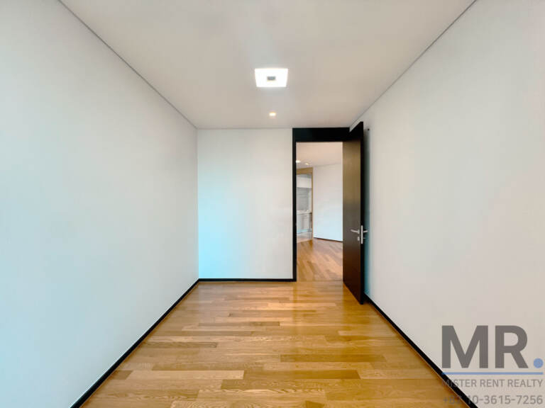 Long white bedroom with oak flooring and dark-framed door