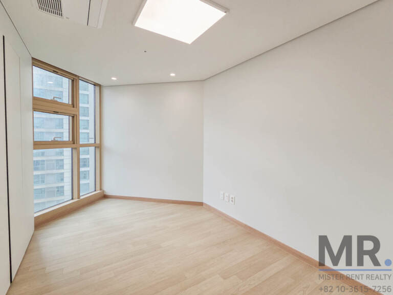 Empty bedroom with tall window overlooking office buildings
