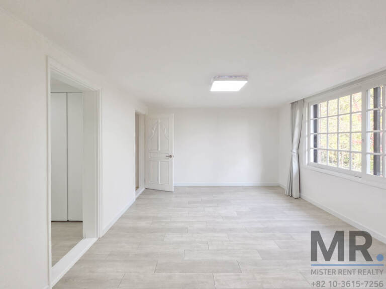 Long bedroom with tile-look floor and windows facing trees