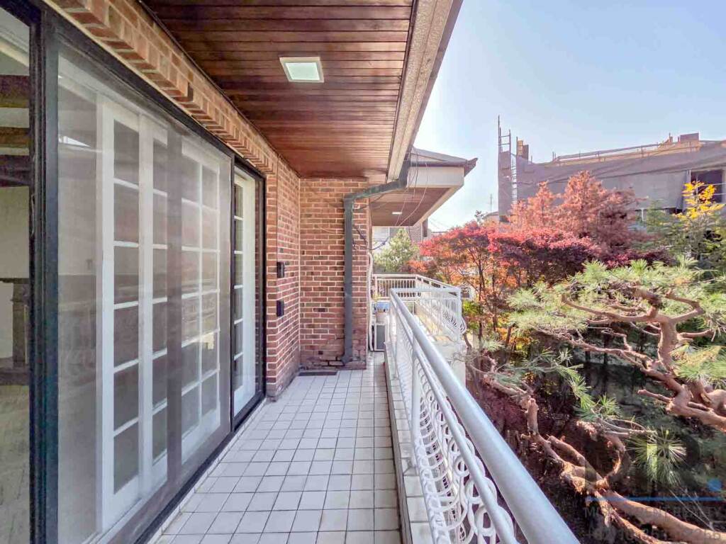 Covered balcony along brick wall with view of pine trees and autumn foliage