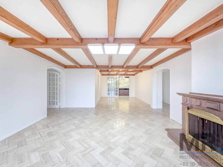 Long living room with exposed wooden ceiling beams, herringbone floor and marble fireplace